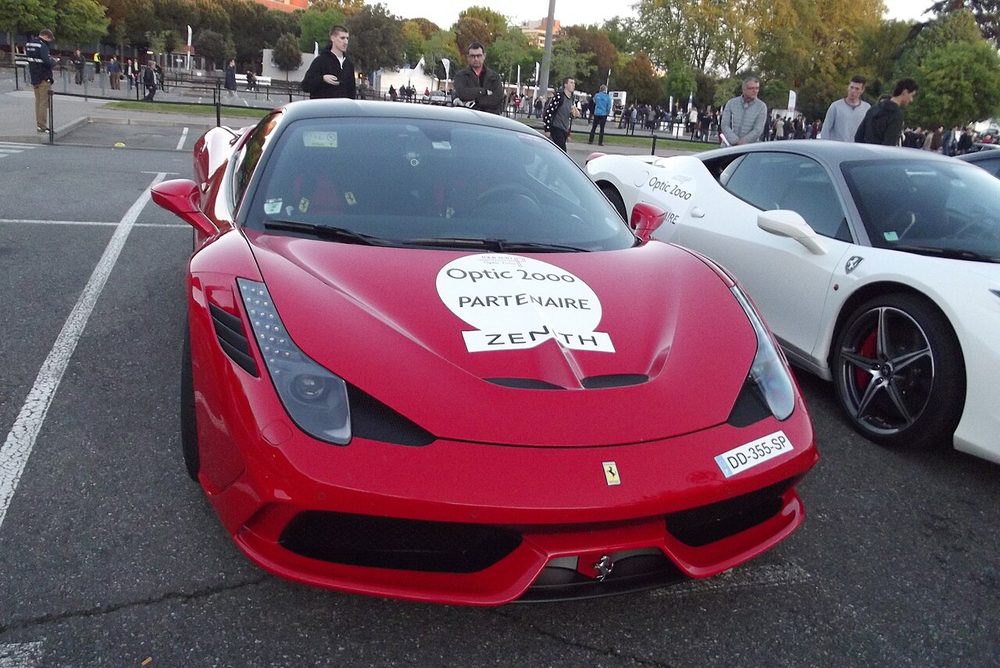 Red Ferrari 458 Speciale with rally event decals parked at the 2015 Tour Auto in Toulouse, next to a white Ferrari